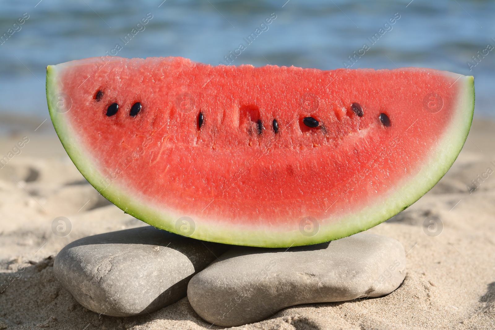 Photo of Slice of fresh juicy watermelon near sea, closeup