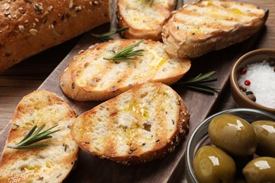 Photo of Tasty bruschettas with oil and rosemary on wooden board, closeup