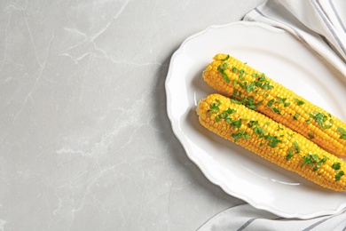 Plate with delicious boiled corn cobs and parsley on light table, top view. Space for text