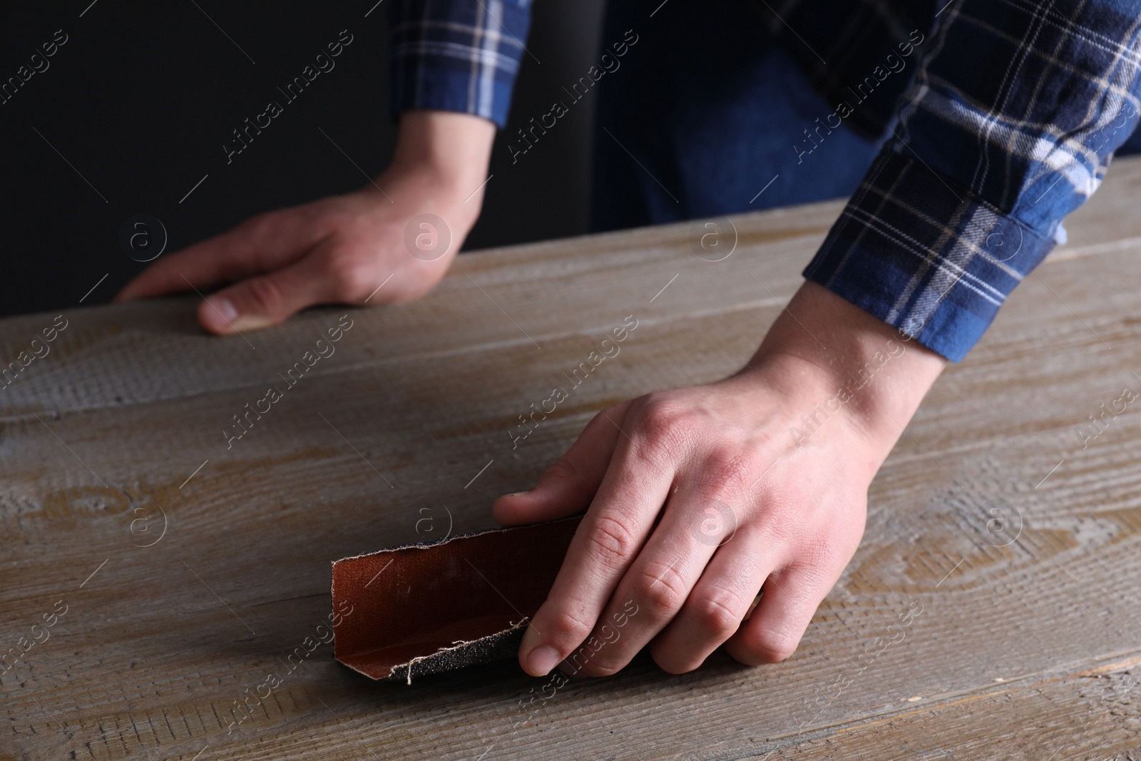 Photo of Man polishing wooden table with sandpaper, closeup