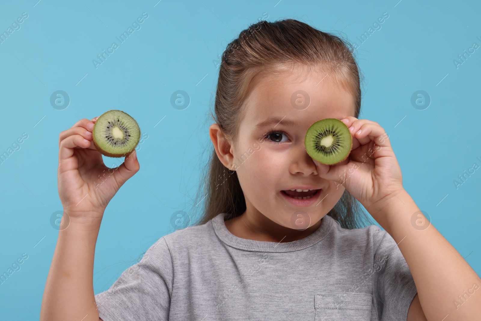 Photo of Cute girl with fresh kiwi on light blue background