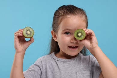 Photo of Cute girl with fresh kiwi on light blue background