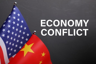 Photo of Phrase ECONOMY CONFLICT, USA and China flags on black background, closeup