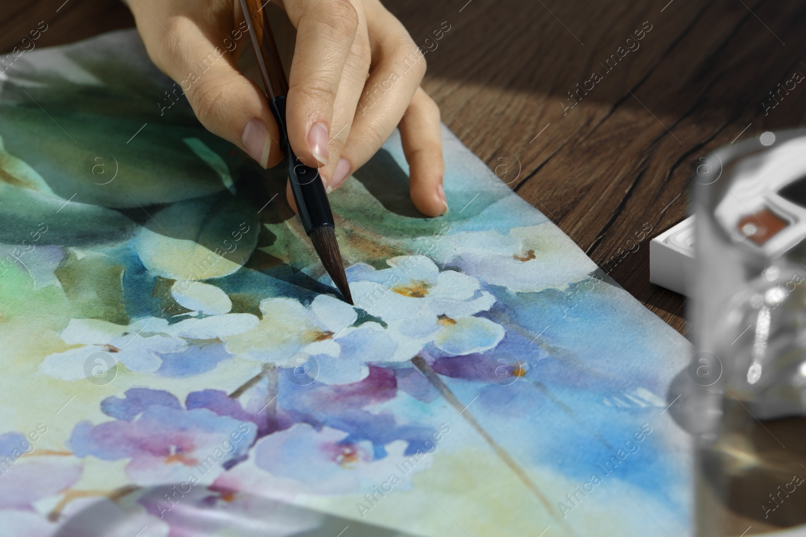 Photo of Woman painting flowers with watercolor at wooden table, closeup. Creative artwork