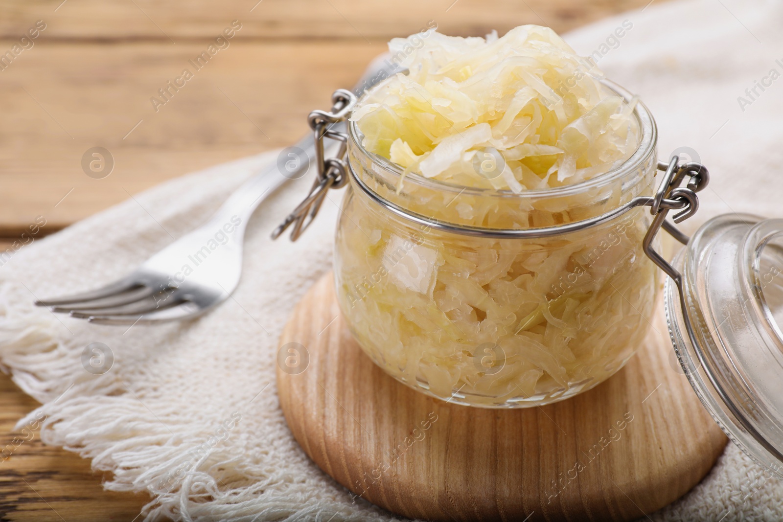 Photo of Glass jar of tasty sauerkraut on wooden table, closeup. Space for text
