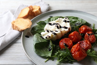 Delicious burrata cheese served with tomatoes, croutons, arugula and basil on white wooden table, closeup