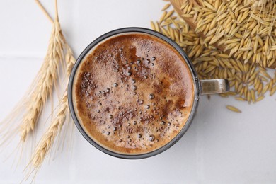 Cup of barley coffee, grains and spikes on white table, flat lay