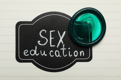 Photo of Green condom and tag with words SEX EDUCATION on paper sheet, top view