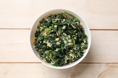 Photo of Tasty spinach dip with eggs in bowl on light wooden table, top view