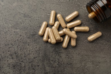 Photo of Overturned bottle with dietary supplement capsules on grey table, flat lay. Space for text