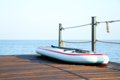 SUP board with paddle on wooden pier near sea