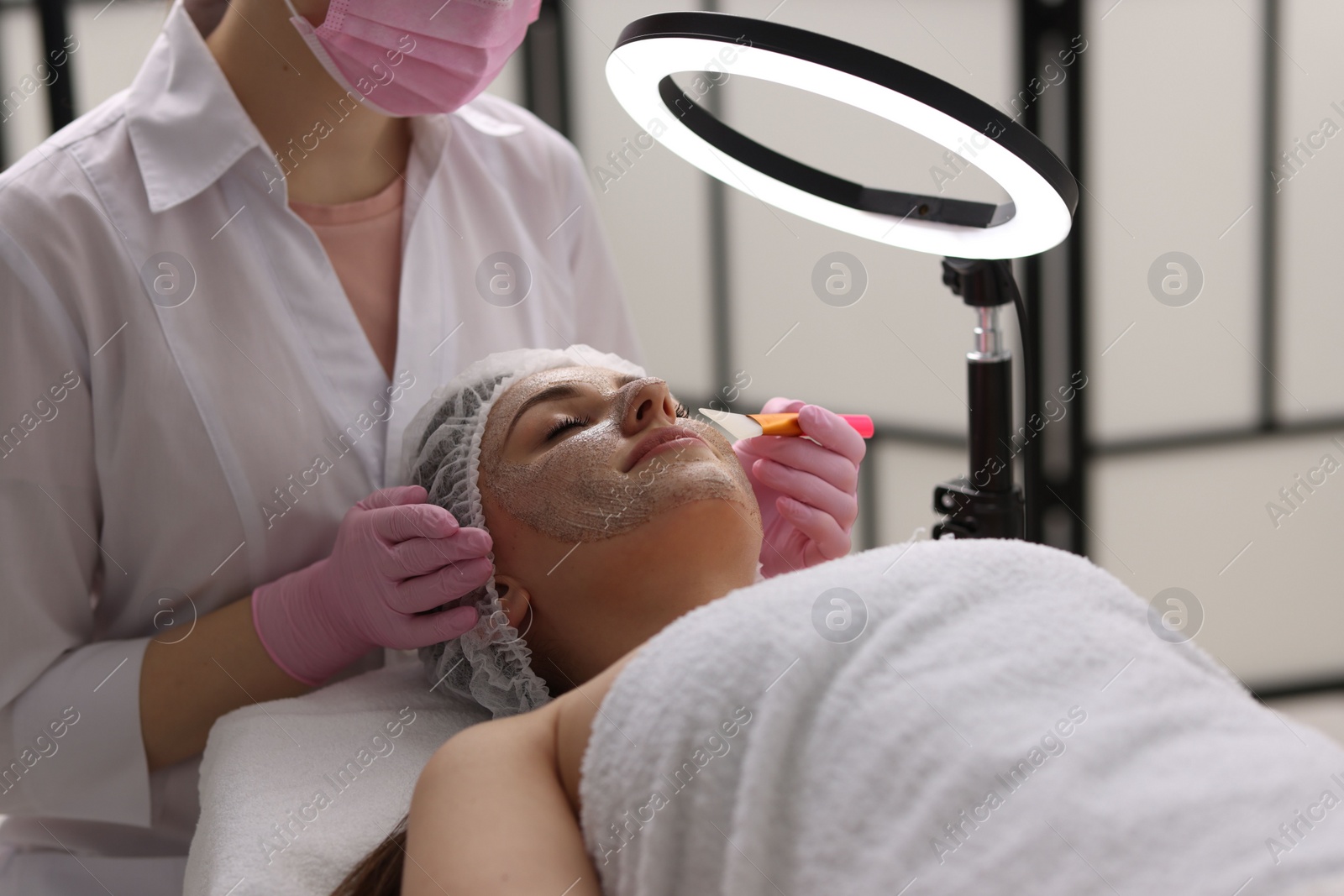 Photo of Cosmetologist applying mask on woman's face in clinic, closeup