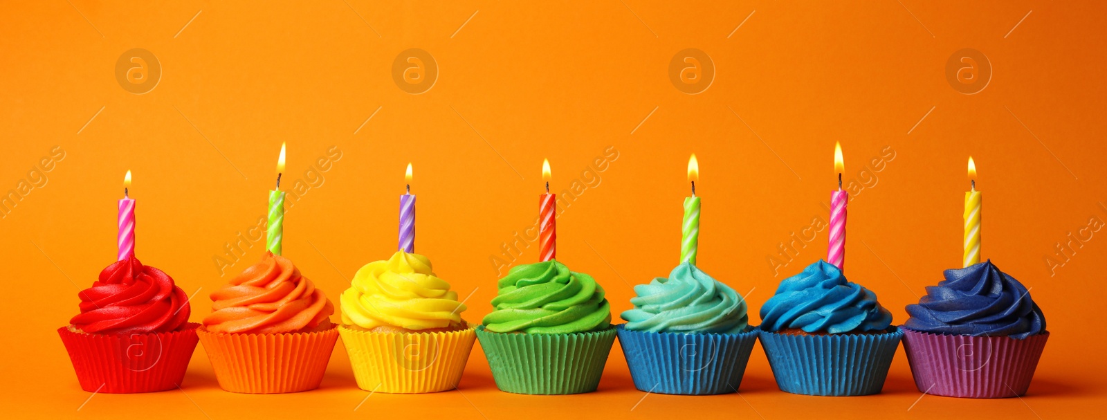 Photo of Delicious birthday cupcakes with burning candles on orange background