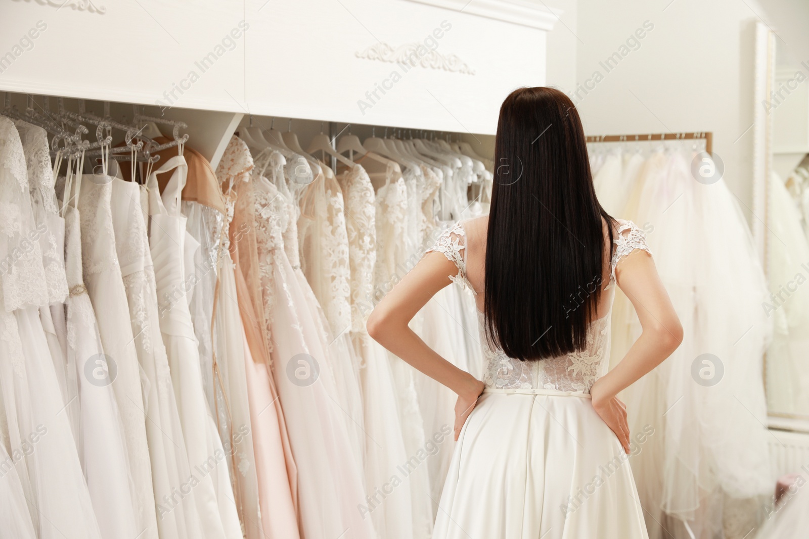 Photo of Woman trying on beautiful wedding dress in boutique, back view