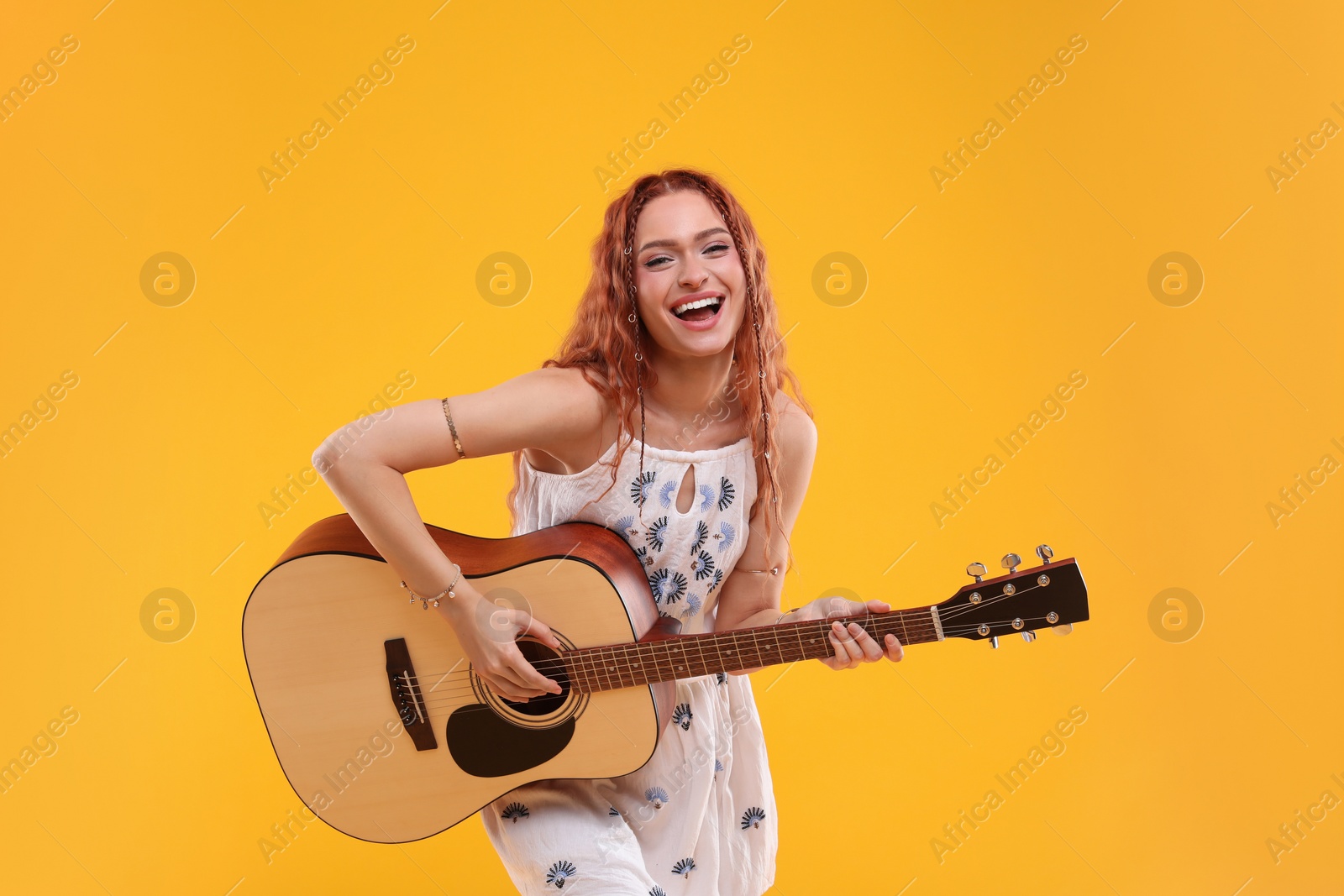 Photo of Beautiful young hippie woman playing guitar on orange background