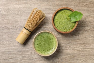 Cup of fresh matcha tea, bamboo whisk and green powder on wooden table, flat lay