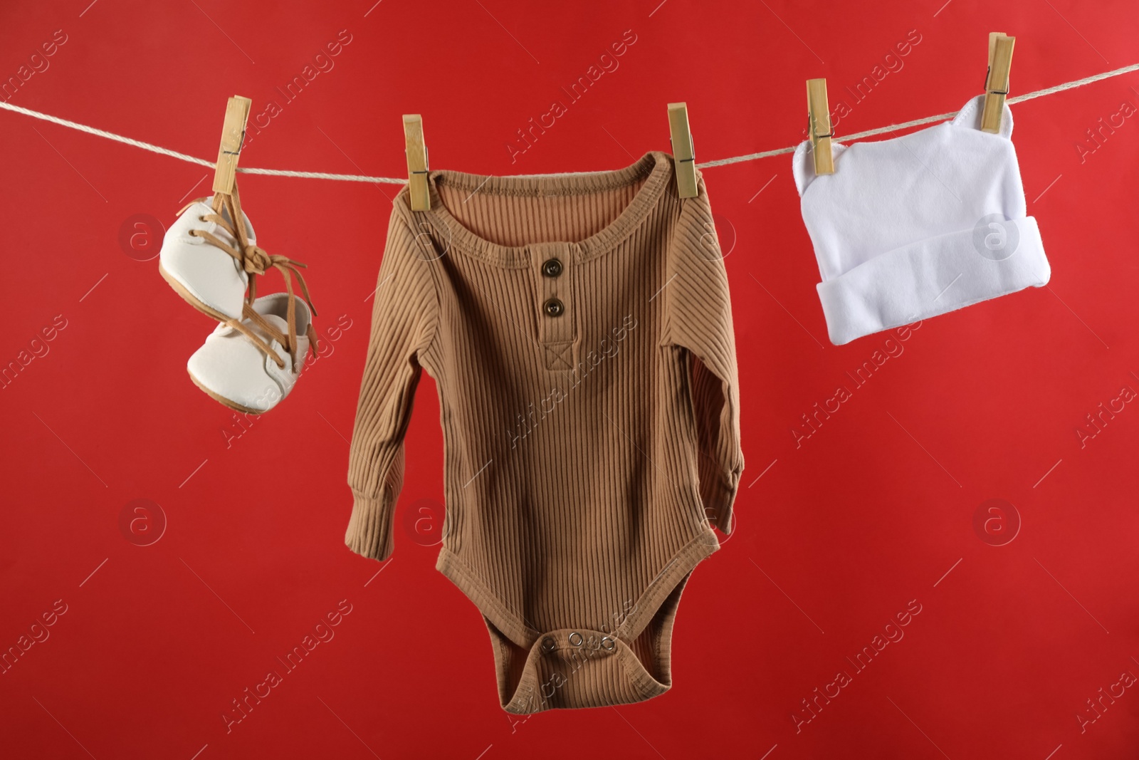 Photo of Baby clothes hanging on washing line against red background