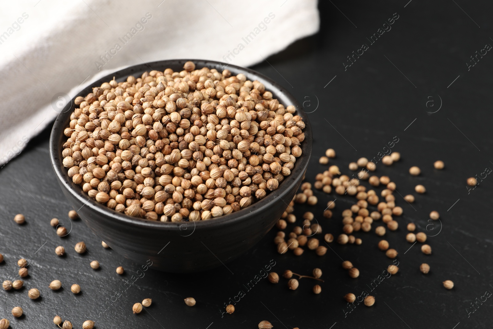 Photo of Dried coriander seeds in bowl on dark gray table, closeup