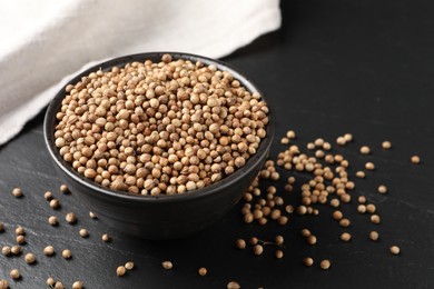 Dried coriander seeds in bowl on dark gray table, closeup