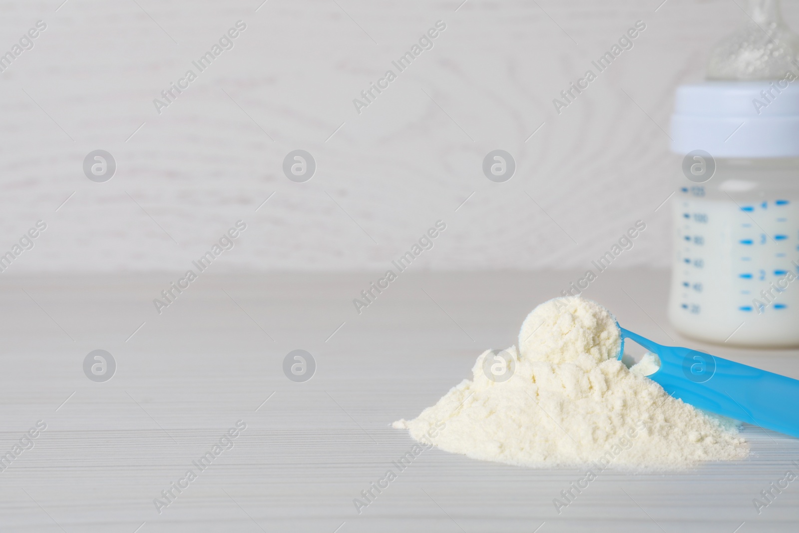 Photo of Powdered infant formula, scoop and feeding bottle on white wooden table, space for text. Baby milk