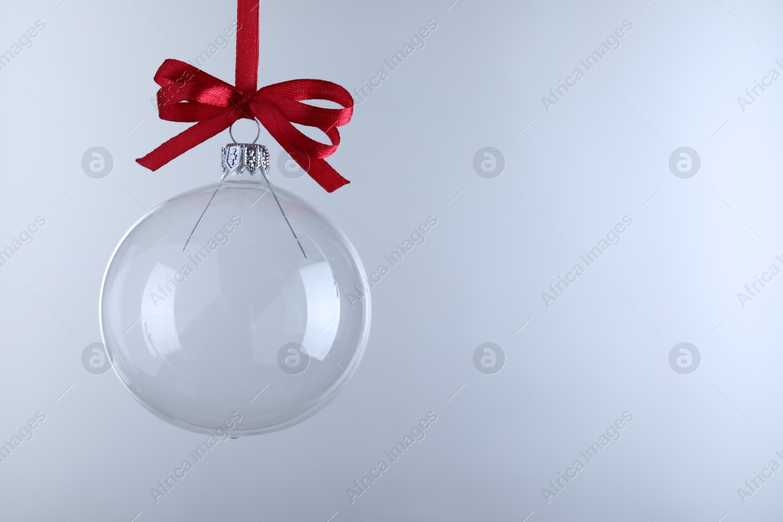 Photo of Transparent glass Christmas ball with red ribbon and bow against light background. Space for text