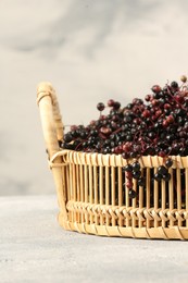 Photo of Ripe elderberries in wicker basket on light grey table