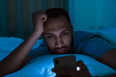 Photo of Young man using smartphone in bed at night. Internet addiction