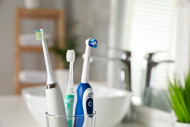 Photo of Electric toothbrushes in glass holder indoors, closeup. Space for text