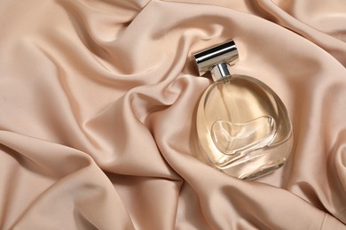 Luxury perfume in bottle on beige silk fabric, top view