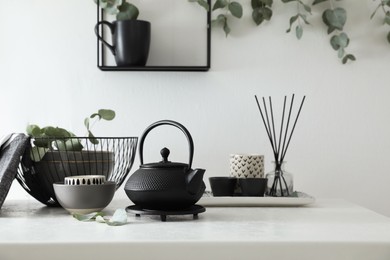 Photo of Stylish black teapot and beautiful green eucalyptus leaves on white table indoors