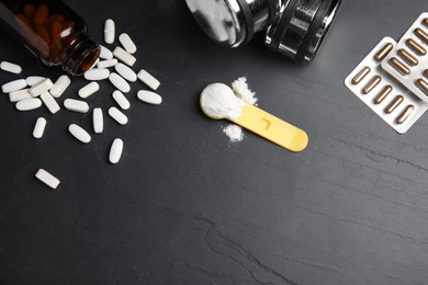 Photo of Pills, measuring scoop of amino acids powder and dumbbells on black table, flat lay