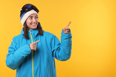 Photo of Winter sports. Happy woman with snowboard goggles pointing at something on orange background, space for text