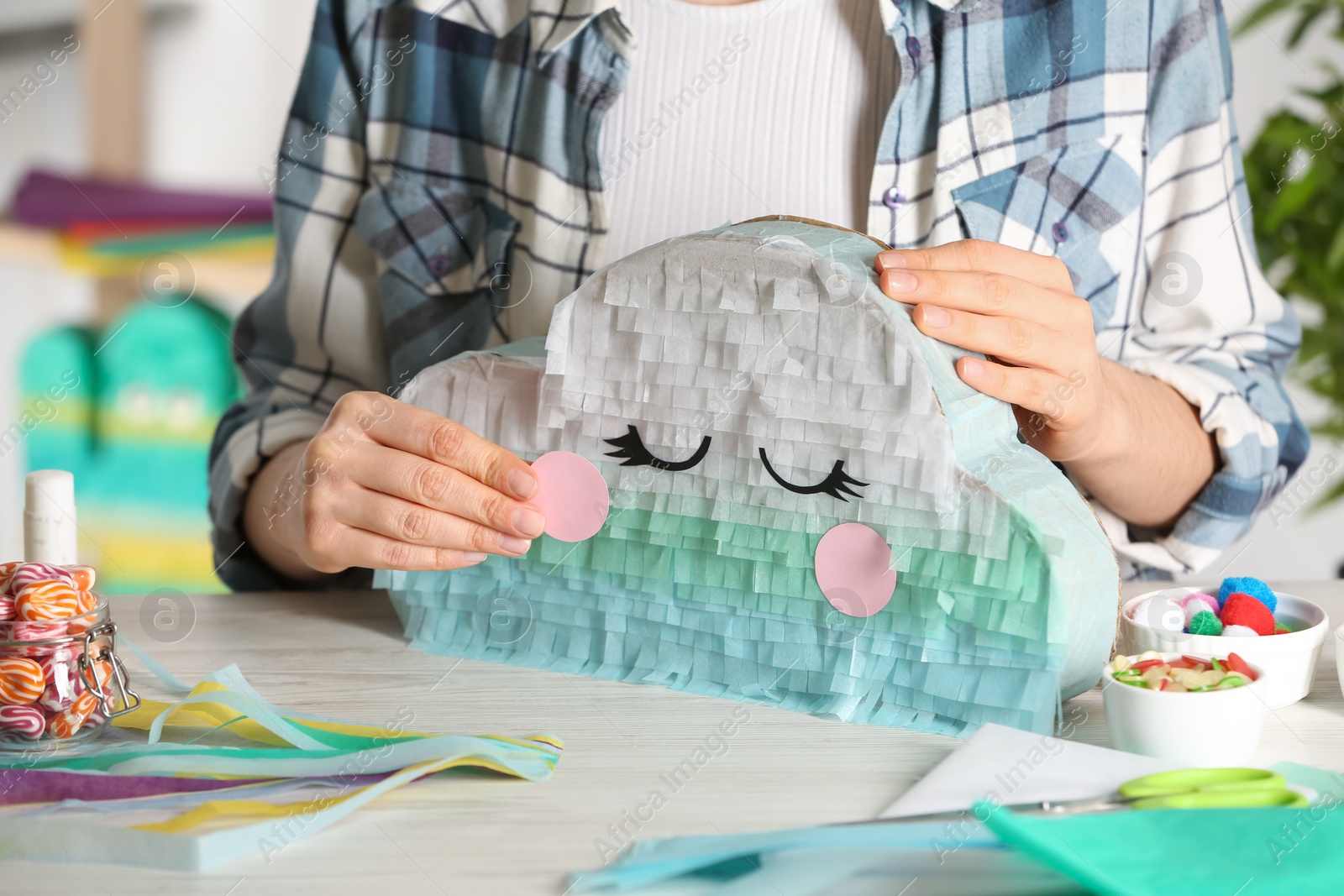 Photo of Woman decorating cardboard cloud at white wooden table, closeup. Pinata diy