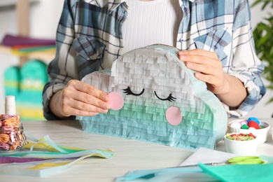 Woman decorating cardboard cloud at white wooden table, closeup. Pinata diy