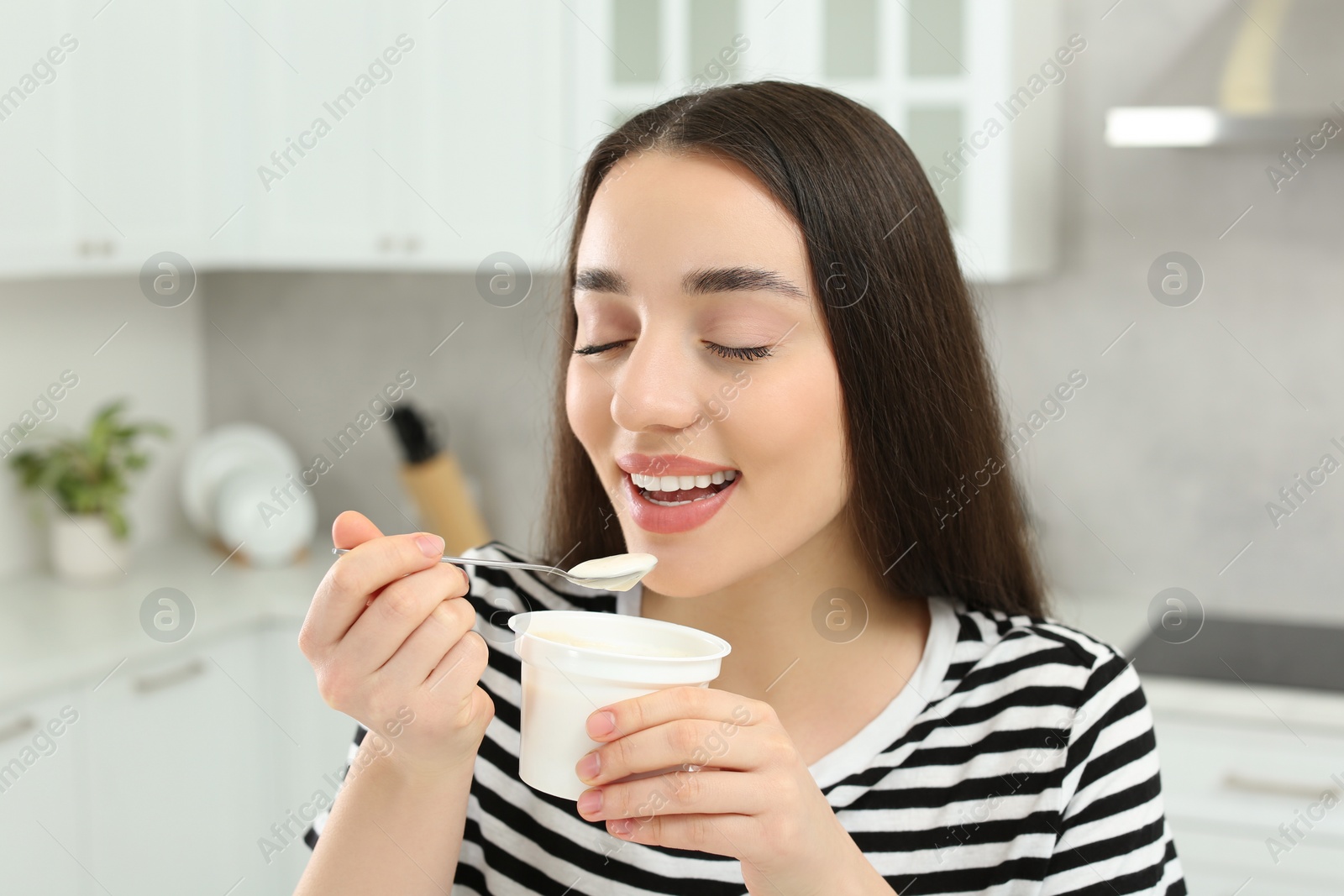 Photo of Happy woman eating tasty yogurt in kitchen