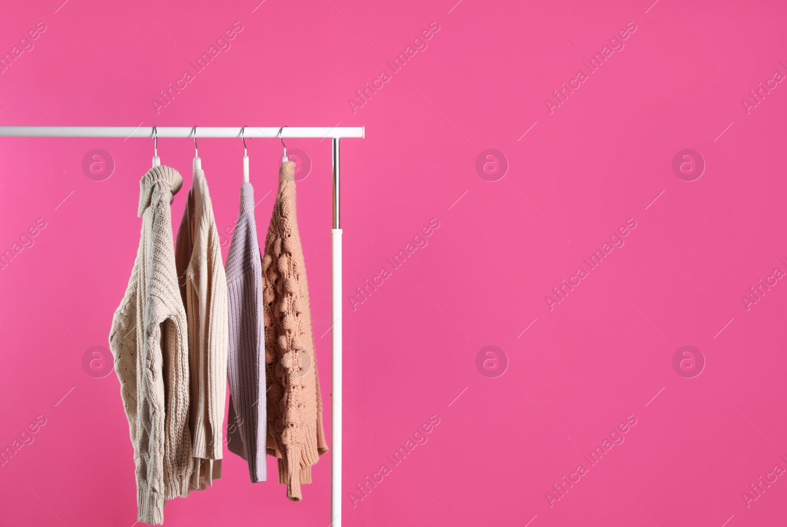 Photo of Collection of warm sweaters hanging on rack against color background. Space for text