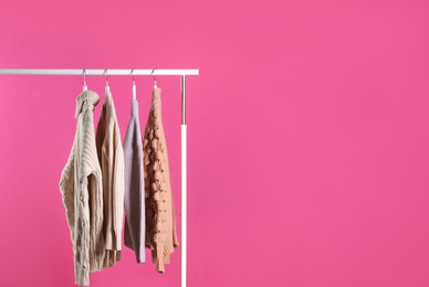 Collection of warm sweaters hanging on rack against color background. Space for text