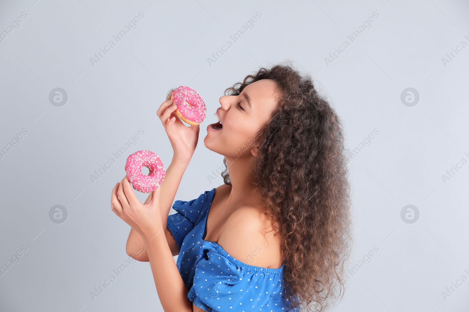 Photo of Beautiful African-American woman with donuts on light grey background