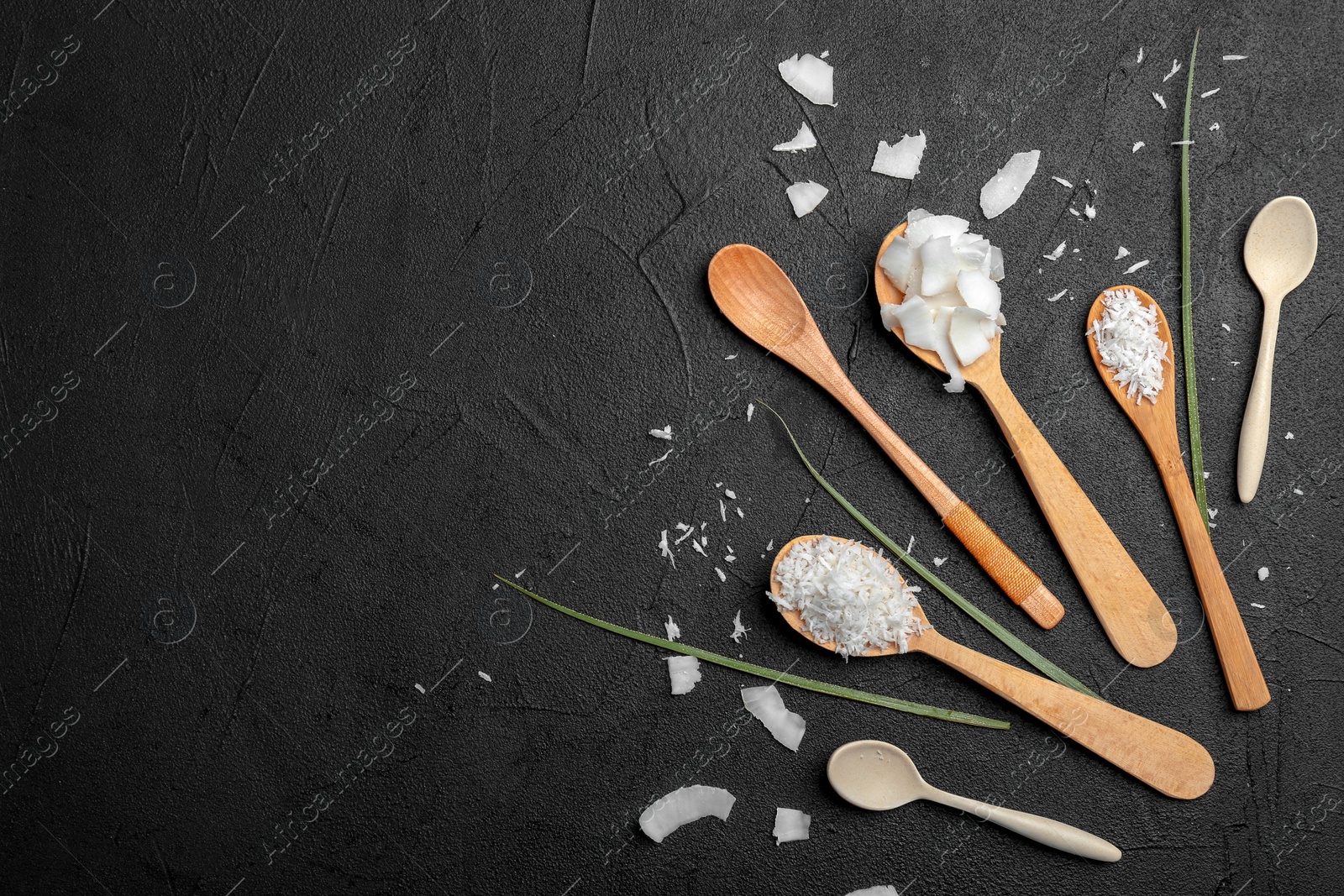 Photo of Wooden spoons with fresh coconut flakes on dark background