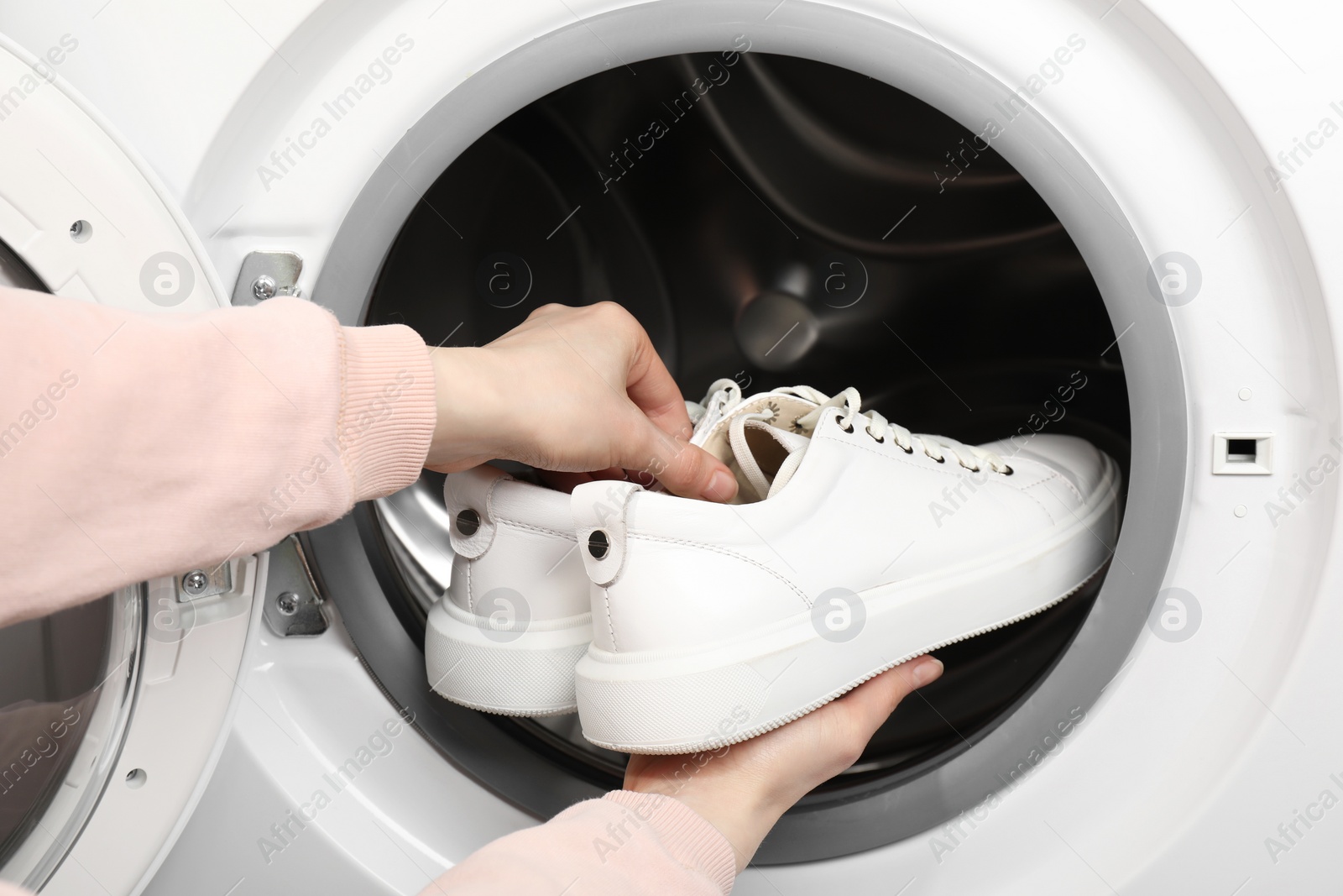 Photo of Woman putting stylish sneakers into washing machine, closeup