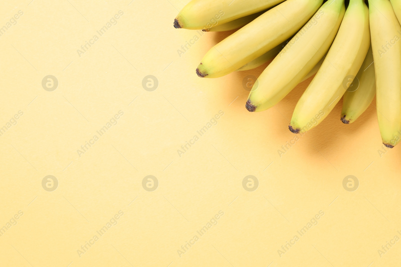 Photo of Bunch of ripe baby bananas on light orange background, top view. Space for text