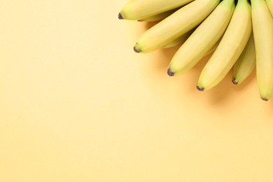 Photo of Bunch of ripe baby bananas on light orange background, top view. Space for text