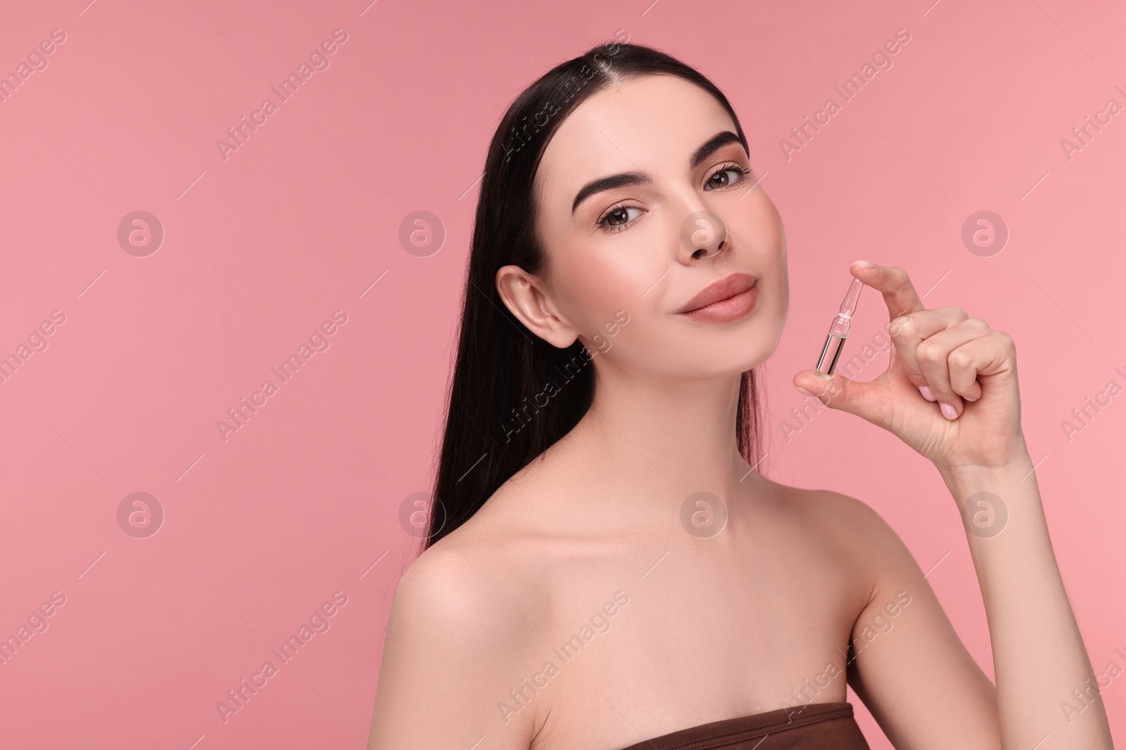 Photo of Beautiful young woman holding skincare ampoule on pink background. Space for text