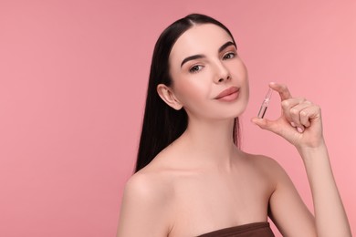 Beautiful young woman holding skincare ampoule on pink background. Space for text