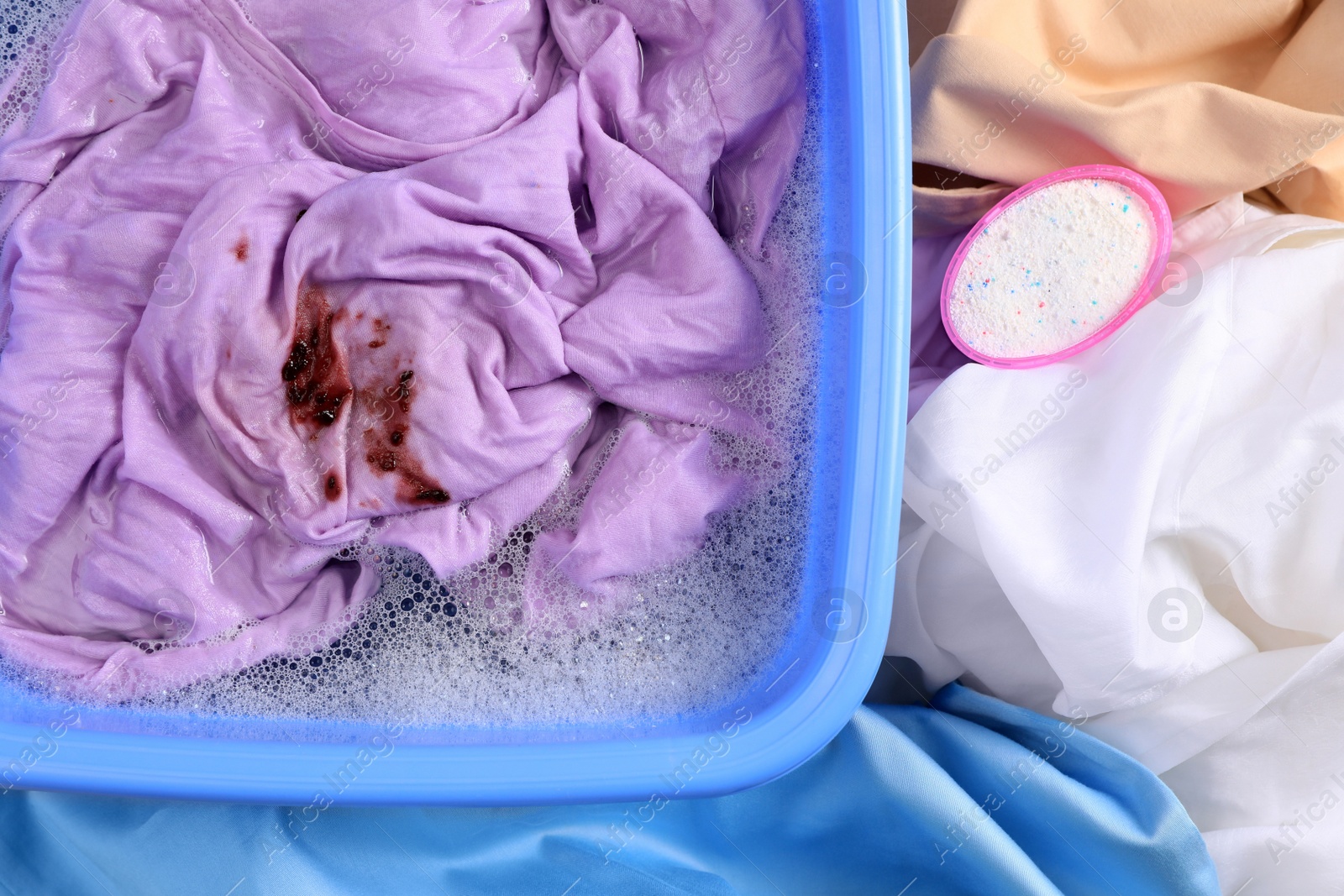 Photo of Garment and powdered detergent near basin with dirty clothes, top view. Hand washing laundry