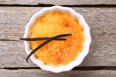 Delicious creme brulee in bowl and vanilla pods on wooden table, top view