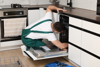 Serviceman repairing dishwasher near toolbox in kitchen