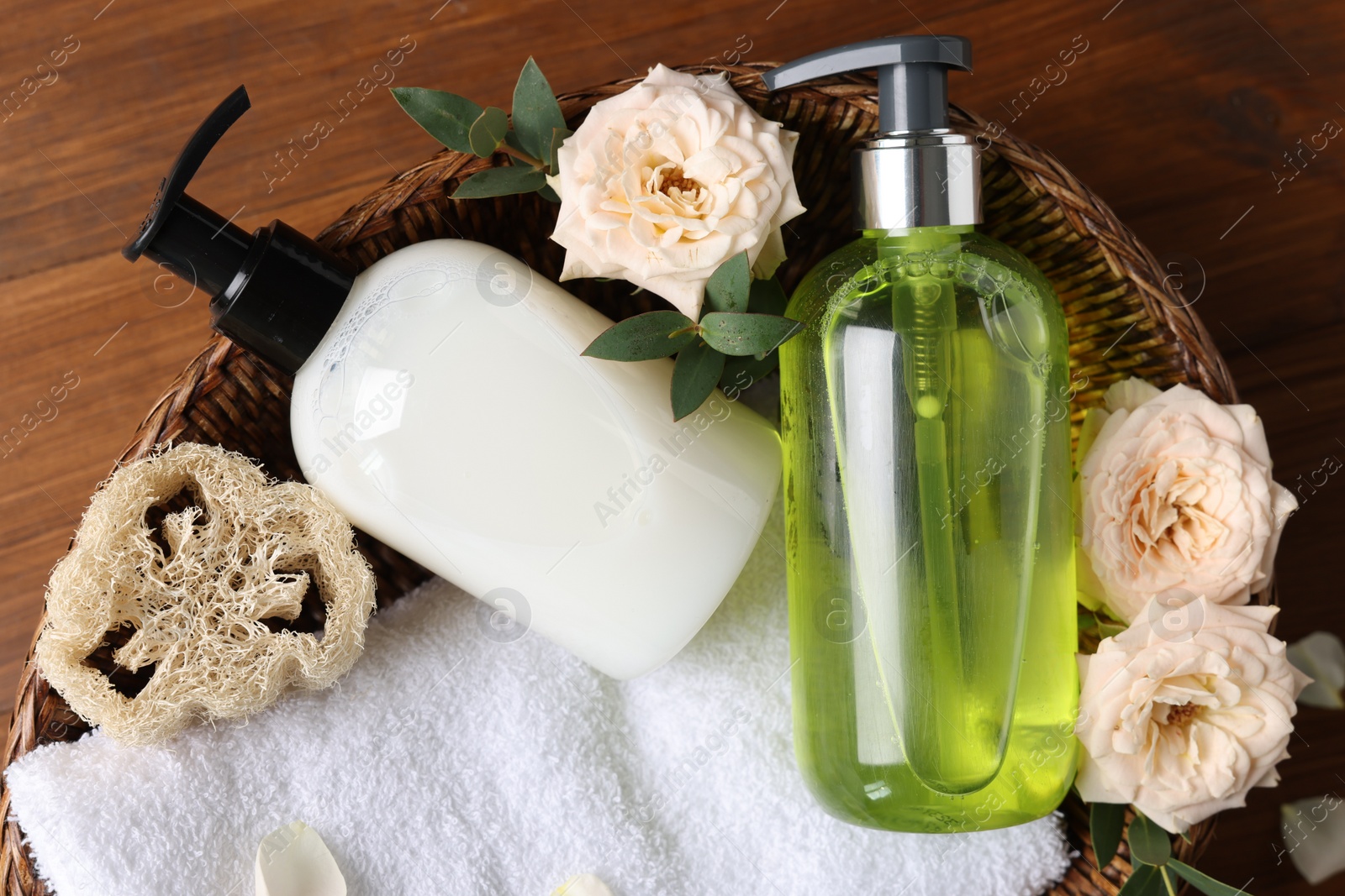 Photo of Dispensers of liquid soap, towel and roses in wicker basket on wooden table, top view