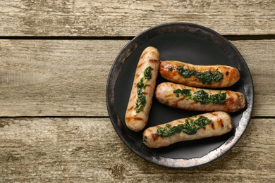Photo of Tasty fresh grilled sausages with sauce on wooden table, top view. Space for text