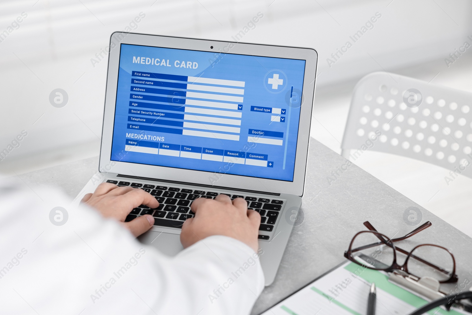 Photo of Doctor using laptop to fill out patient's medical card at table in clinic, closeup